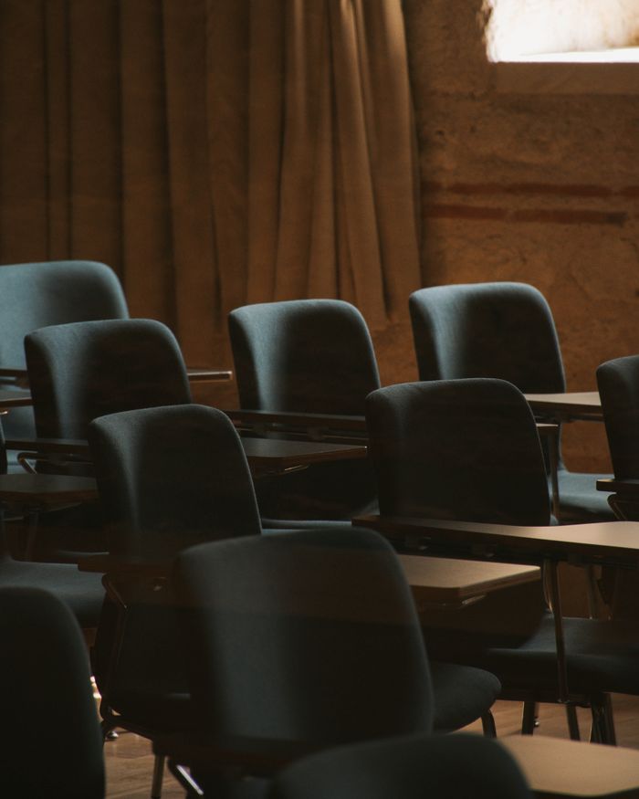 A dimly lit empty classroom with multiple rows of chairs and tables, suggesting a moment of calm before or after class.